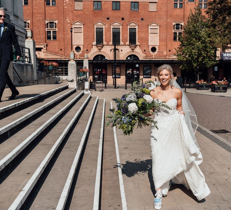 Bride walks and lifts up wedding gown on the way to venue