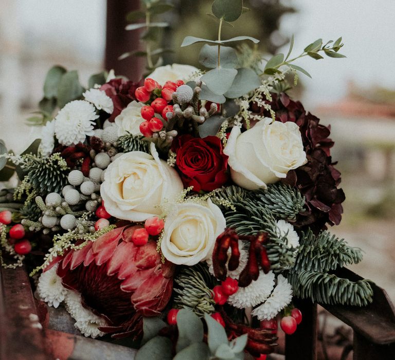 A bouquet of red and white roses, eucalyptus and pine leaves, berries and seasonal blooms