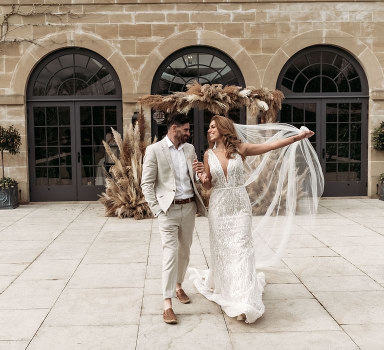 Bride and groom standing in front of a pampas grass installation with earthy wedding decor 