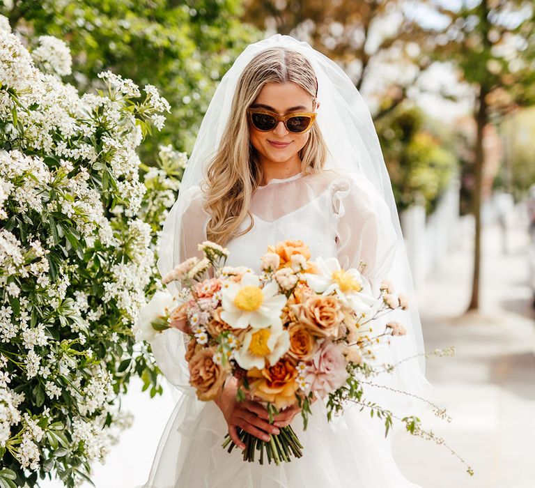 Stylish bride in sunglasses and a short ruffle wedding dress holding a yellow wedding bouquet 