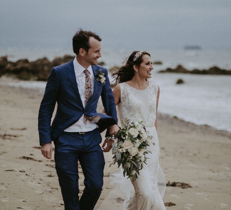 Bride & groom walk together along the beach on their wedding day