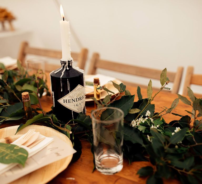 Botanical wedding tablescape with wooden plates, foliage table decor and Hendricks gin bottle with white candle