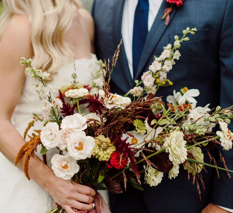 Bride and groom smiling at their Italy elopement, the bride is holding a bouquet of white, red and neutral toned flowers