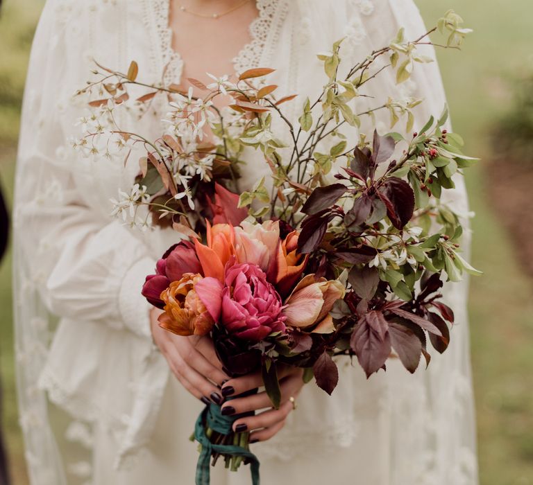 Bride in Charlie Brear wedding dress and applique veil holds multicoloured wedding bouquet with foliage and white flowers at garden party wedding in Devon