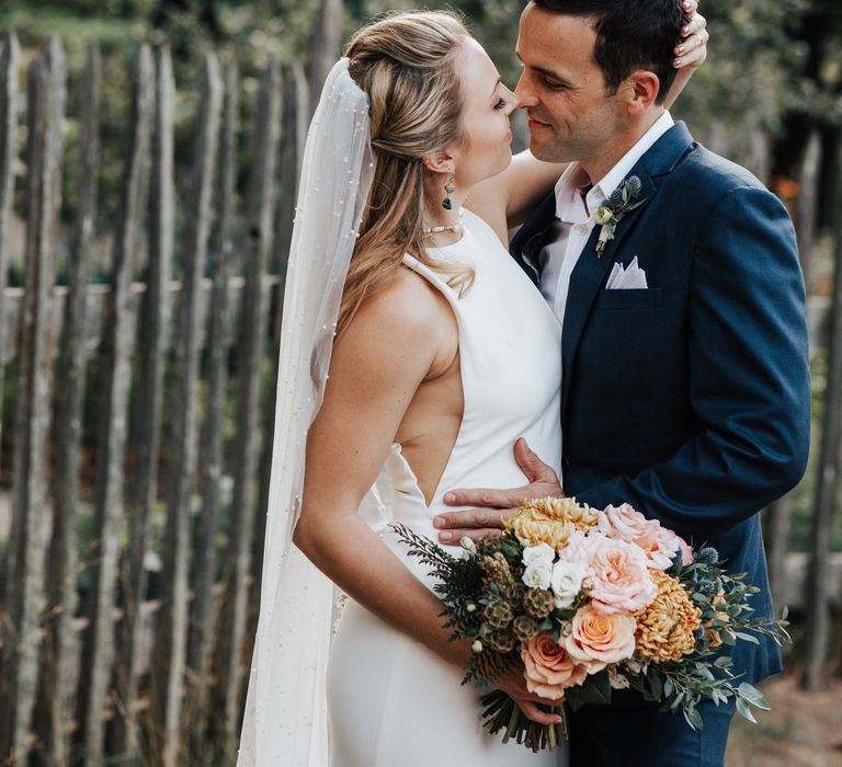 Groom leans in to kiss blonde bride as she wears pearl bouquet