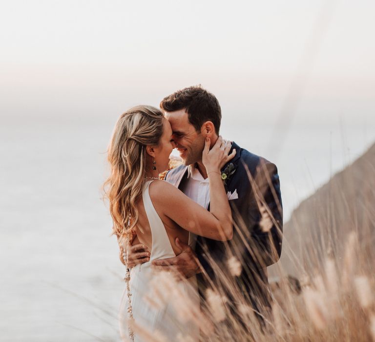 Bride & groom lean in to one another outdoors on the cliffside 