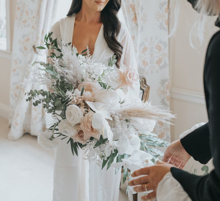 Bride with long dark curled wedding hair and long white bridal dressing gown holds pink, white and green wedding bouquet in bedroom at Came House Dorset Wedding