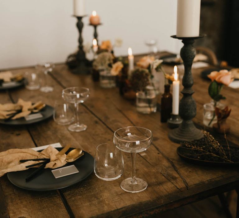 Minimal, rustic, luxe tablescape with black tableware, pillar candles, and dried foliage