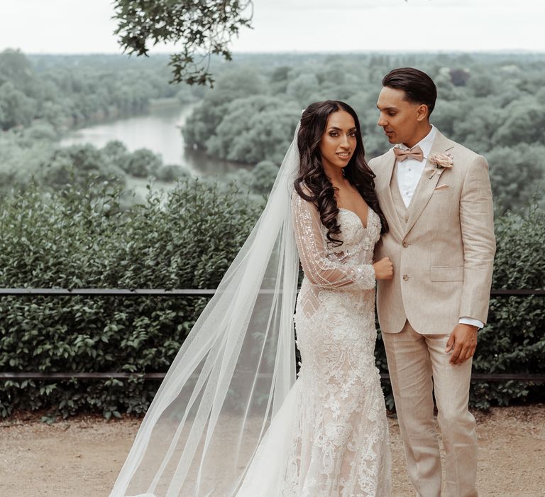 Bride & groom stand outdoors as bride wears Mille Nova wedding gown