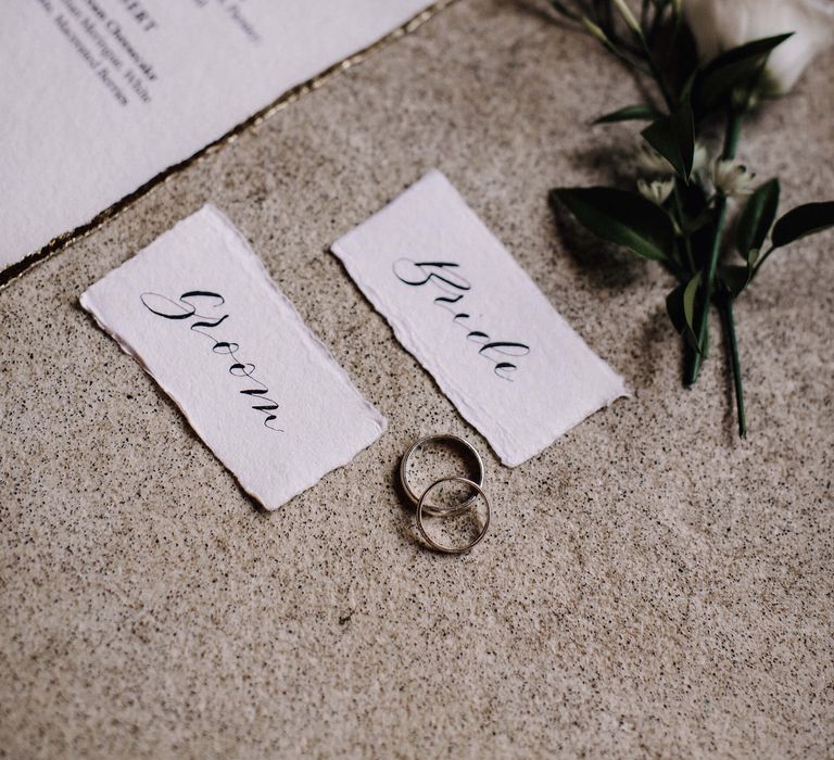 Gold edged wedding stationery with bride and groom name tags next to their wedding bands