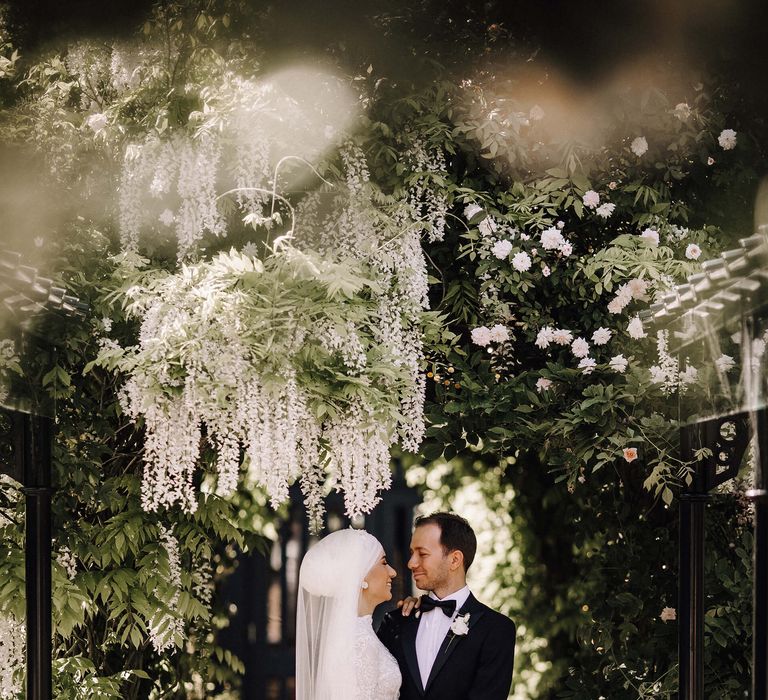 Bride and groom under wisteria with white rose and orchid wedding bouquet 