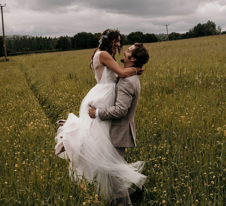 Groom lifts bride in green field on the day of their wedding