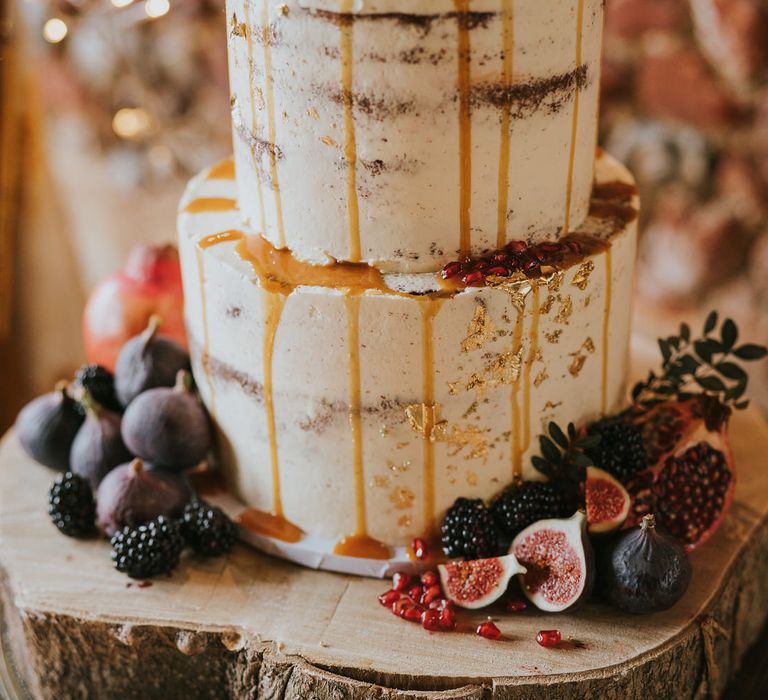 Two tier naked iced wedding cake with dripping caramel sauce, fig and berry decorations on wooden tree trunk cake stand