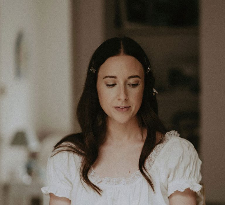 Bride in white puff sleeve dress sits with clips in her hair as she prepares for her summer wedding in Surrey