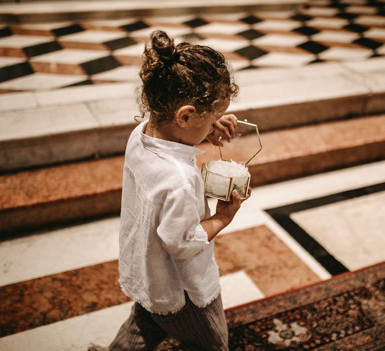 Little boy wears his curly hair in bun and carries a little glass box