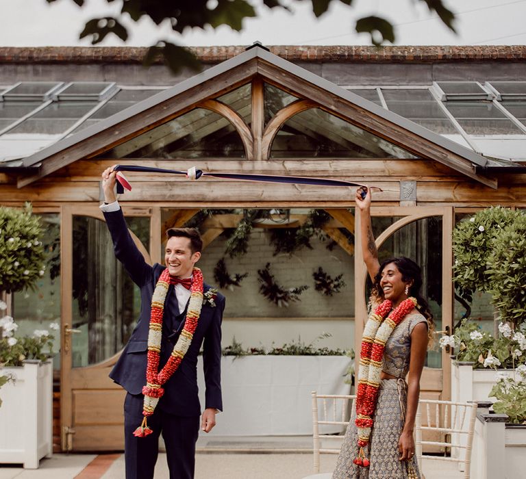 Bride & groom laugh and smile as they hold up tied ribbon above their heads during ceremony  | Joshua Gooding Photography