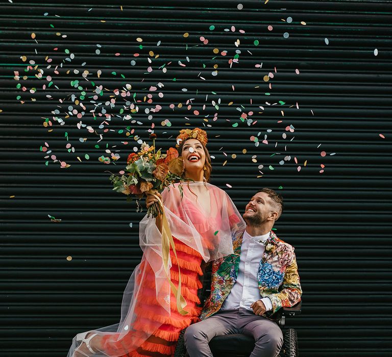 Colourful confetti wedding portrait of interabled couple with bride in a coral wedding dress and disabled groom in a colourful jacket 