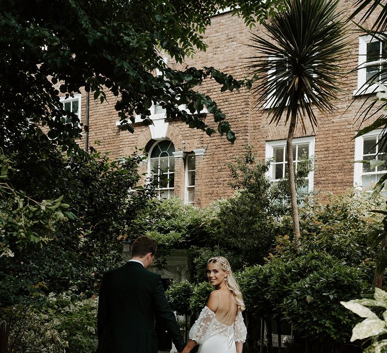 Bride and groom holding hands with bride in a satin and lace wedding dress with spaghetti straps 