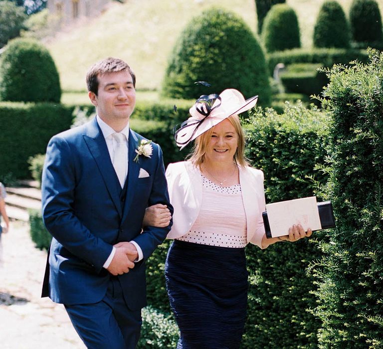 Groom in a navy three-piece suit and white tie with the mother of the groom in a white and navy dress