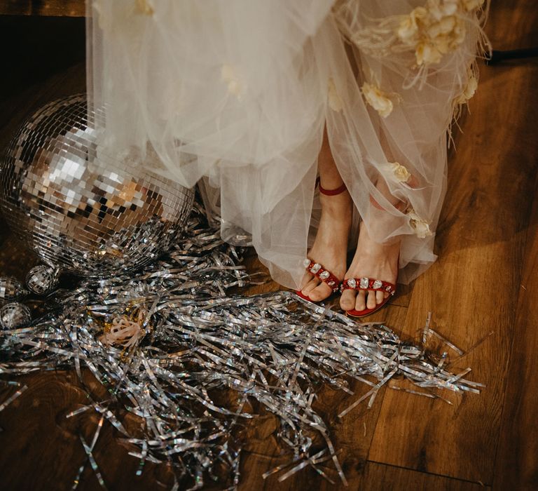 Bride in tulle wedding dress lifts up skirt to show red heeled sandals at rustic wedding in Lancashire