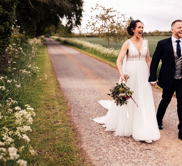 Newlywed bride and groom walk hand in hand through the grounds of Cripps Barn 