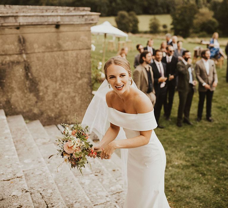 Bride wears off the shoulder bridal gown and holds floral bouquet