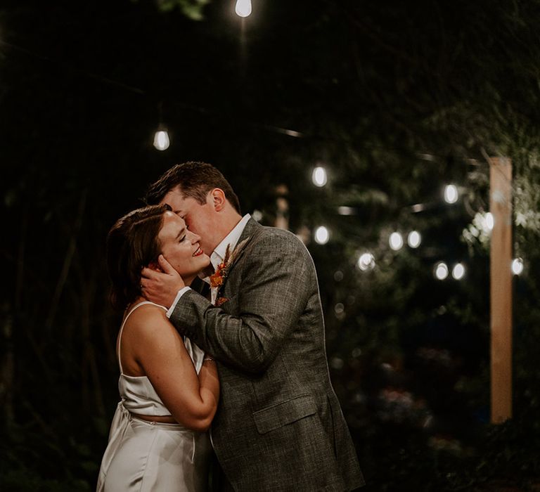 Groom in a grey suit kissing his brides cheek 