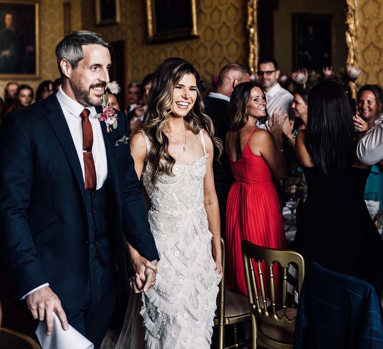 Bride & groom smile as they walk through wedding guests