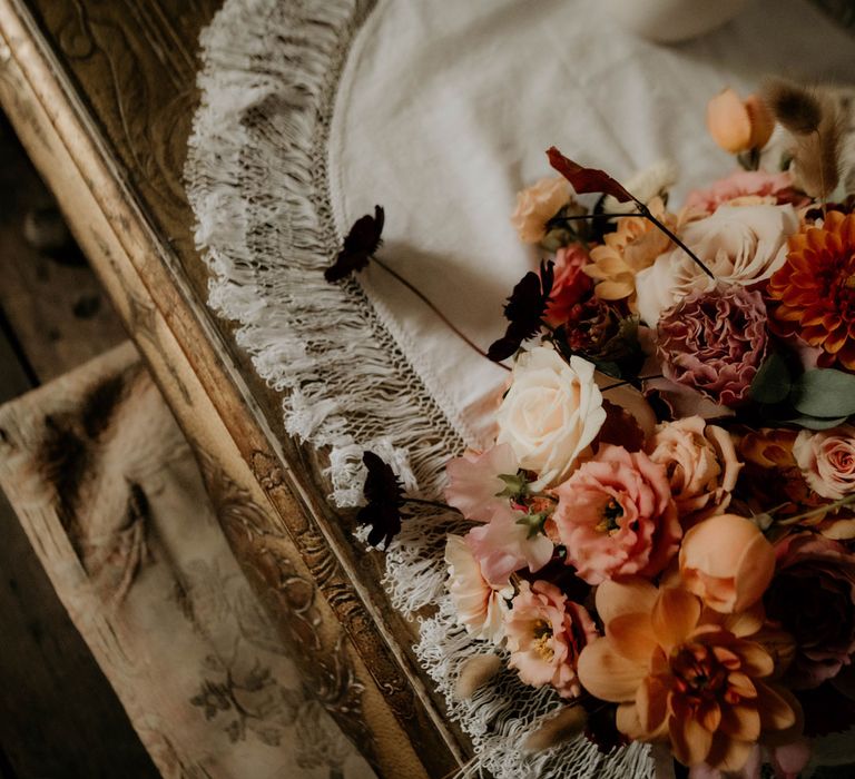 Dusky pink, orange and white mixed bridal bouquet on wooden table before wedding