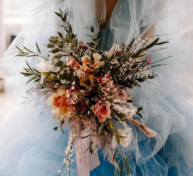 Bride in a blue tulle wedding dress holding a peach flower and green foliage wedding bouquet 