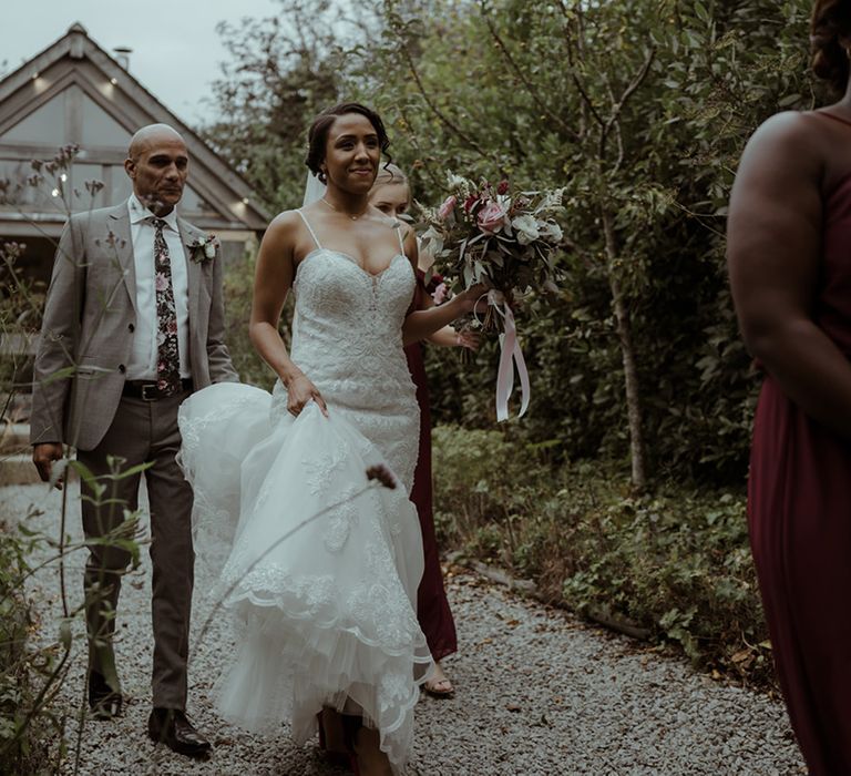 Bride holds her gown as she walks to wedding ceremony in Cornwall 