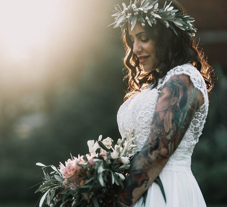 Bride wears floral crown and has her sleeve tattoo on show in boho chic gown with capped sleeves 