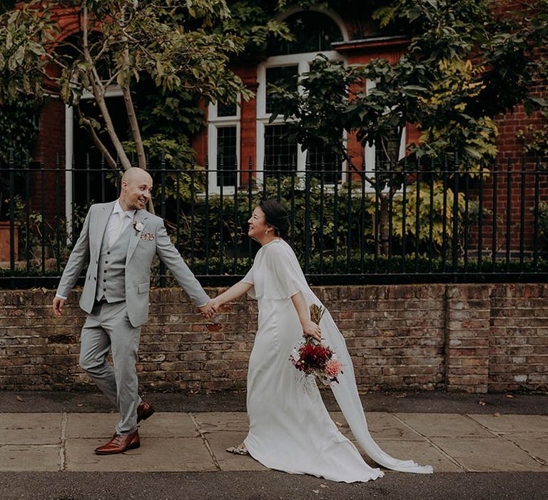 Groom leads his bride as they walk through streets on their wedding day