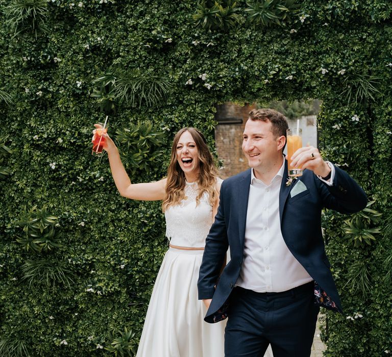 Bride and groom enter their reception holding alcoholic beverages ready to celebrate