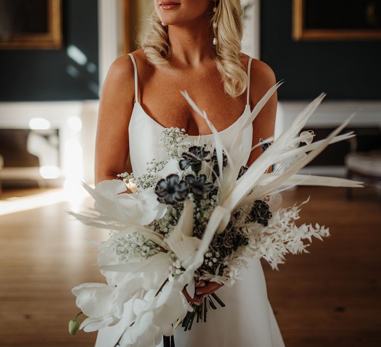 Blonde bride with long wavy hear wearing pearl earrings and holding a dried and fresh flower boqueut with orchids 