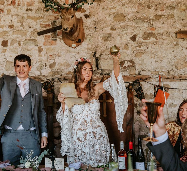 Bride and groom on large wooden thrones get the wedding guests to raise their golden goblets in a toast 