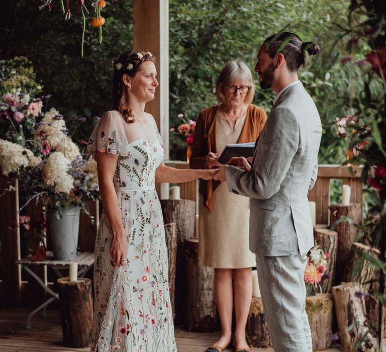 Bride in floral embroidery wedding dress and groom in grey suit at the altar with hanging mini pumpkin decoration and flower decorations for botanical wedding 