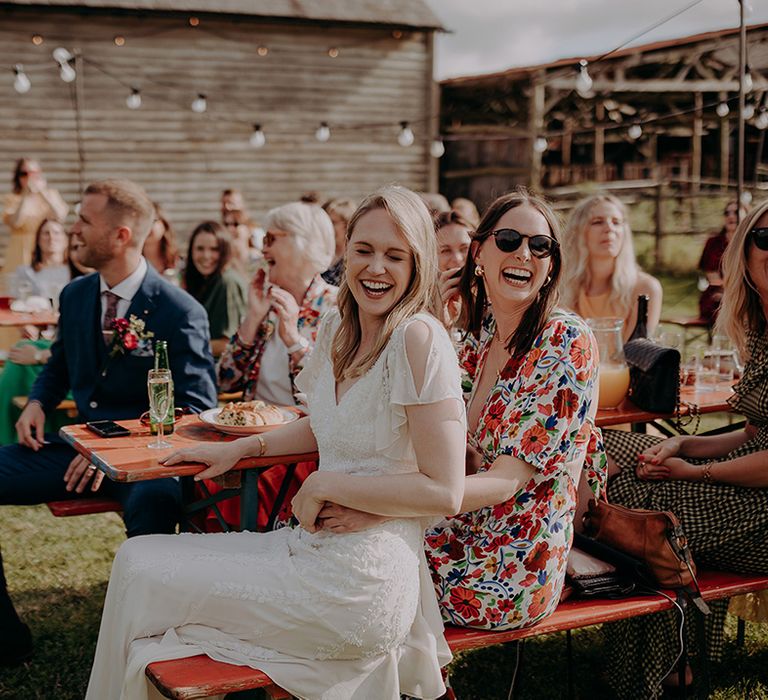 Guests and bride and groom sit together on red benches outside to listen to the speeches