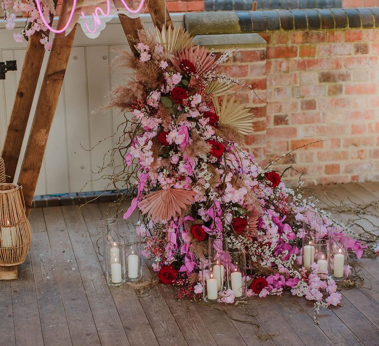 Wedding flower arrangement with pink cherry blossom, dried palm leaves, pampas grass and roses surrounded by pillar candles 