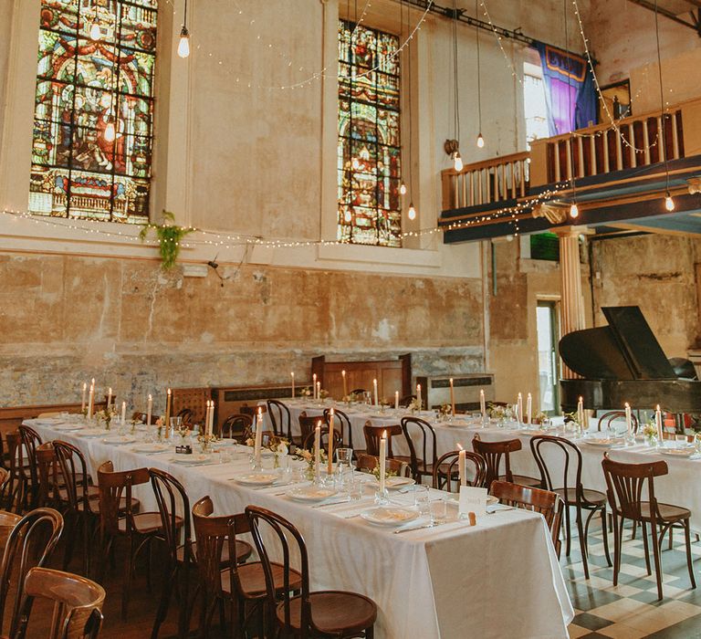 Freud wedding reception venue with fairy lights, stained glass windows, black piano and white tablecloths on banquet tables 