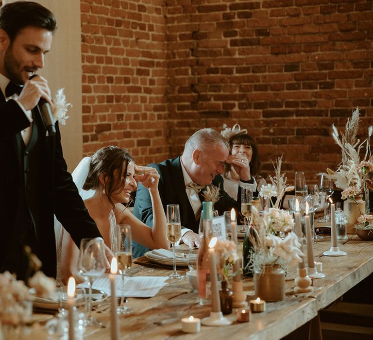 Groom makes his speech as the bride and father of the bride laugh 