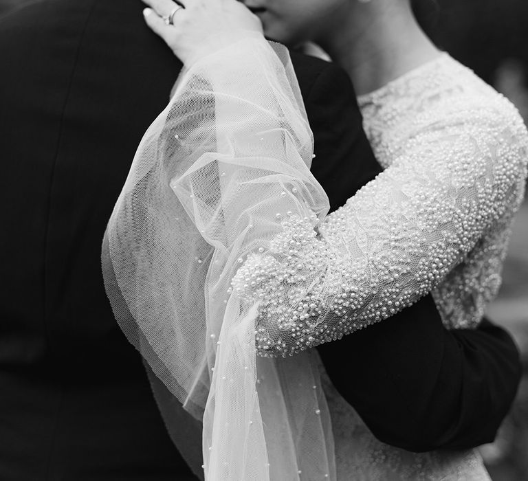 Bride in a beaded wedding dress with bell sleeves embracing her groom in a tuxedo 