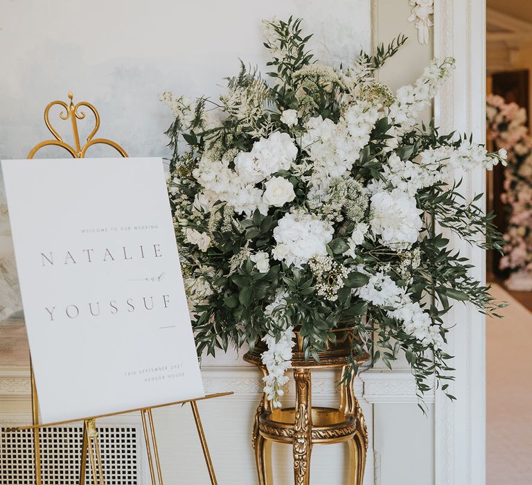 Classic black and white welcome wedding sign on gold easel with white flowers including stock for traditional country house wedding 