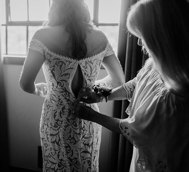 Mother of the bride helps zip the bride into her fitted lace wedding dress 