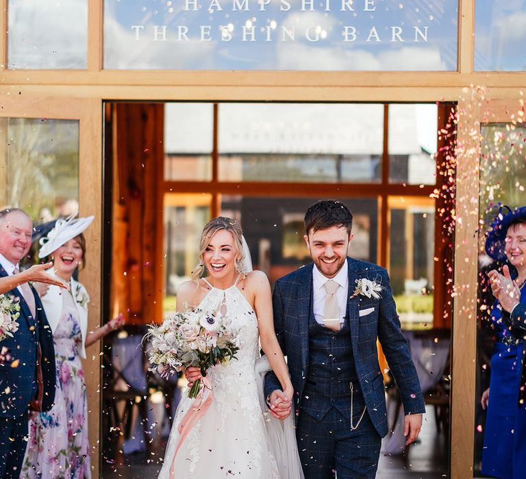 Bride and groom holding hands exit their wedding ceremony to colourful confetti 