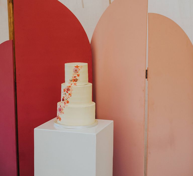 Three tier frosted wedding cake with colourful minimal flower design in front of the pink wedding screen background 