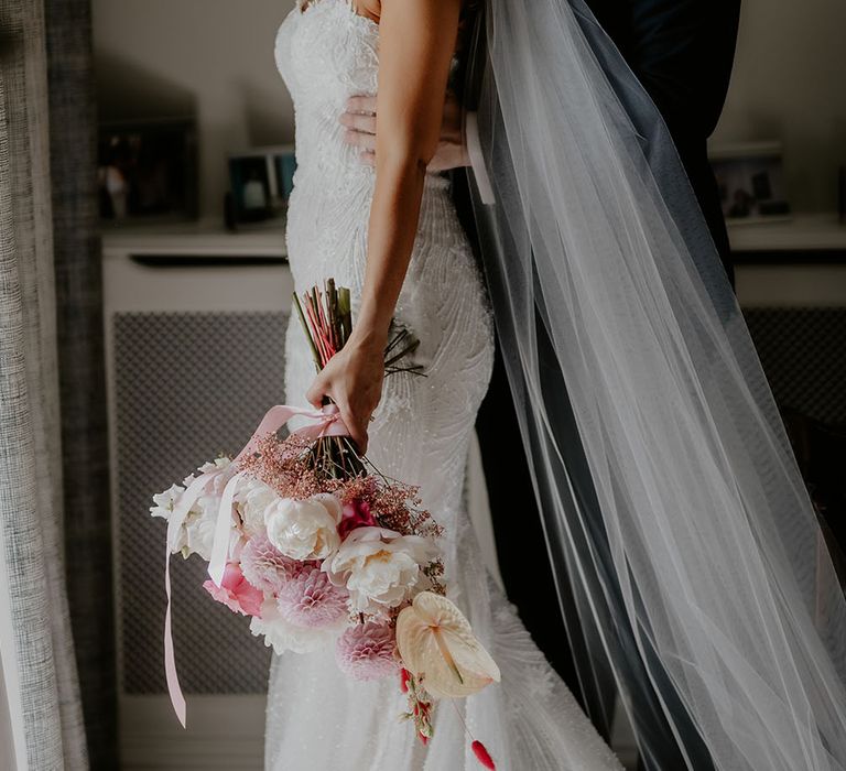 Bride holds white and pink floral bouquet tied with pastel pink ribbon 