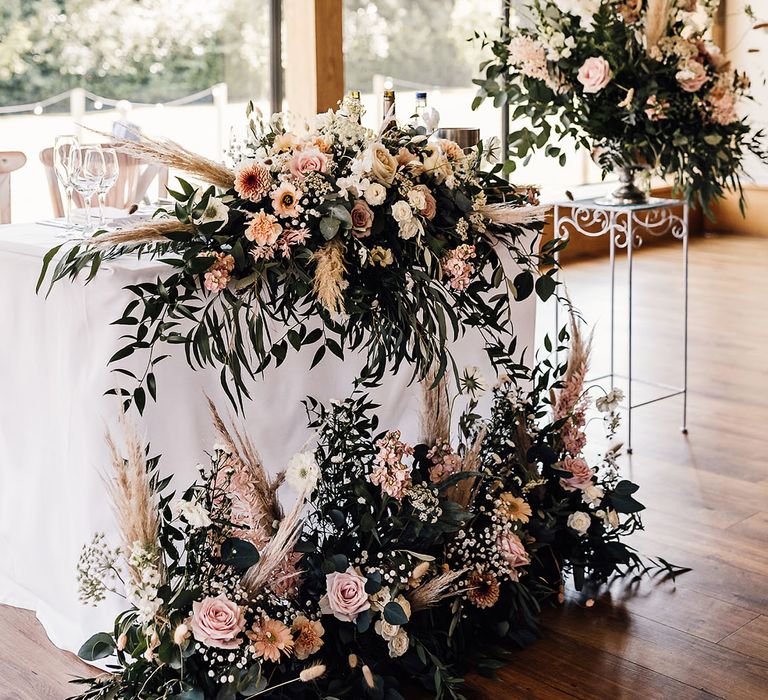 Pastel pink and neutral toned flower arrangements with green foliage and pampas grass