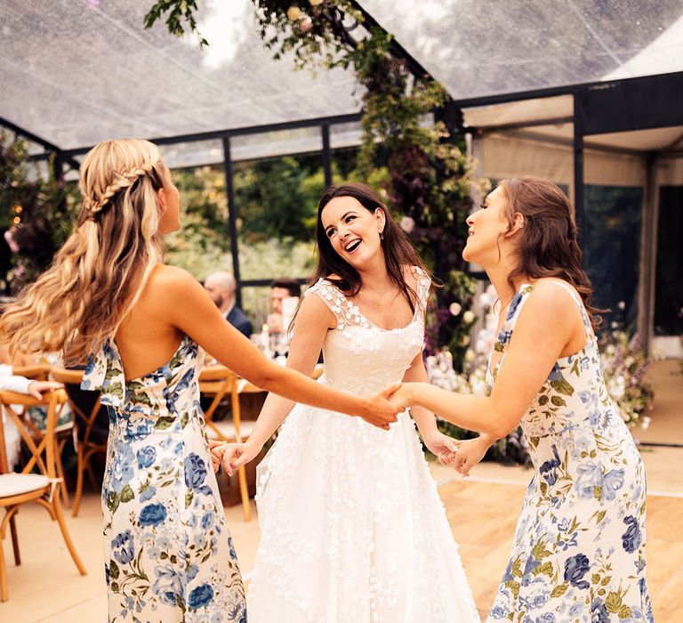 Bride dances with her bridesmaids holding hands in blue and white floral dresses 