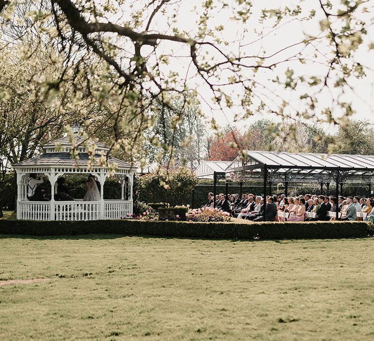 Wedding guests sit outside under cover for the outdoor wedding ceremony 